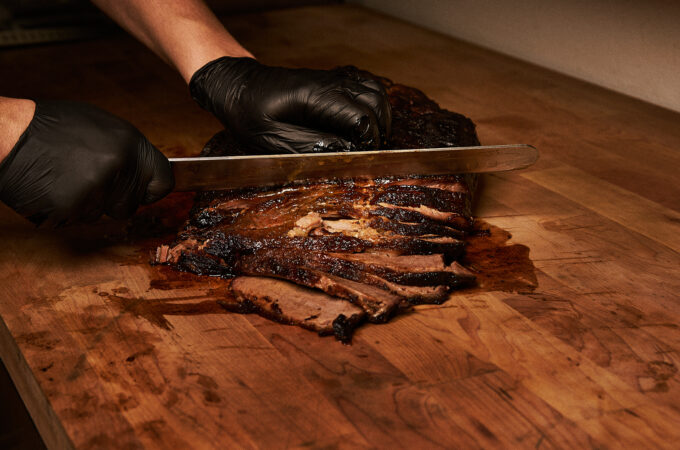Chef slicing smoked brisket on wooden cutting board for fusion BBQ dish