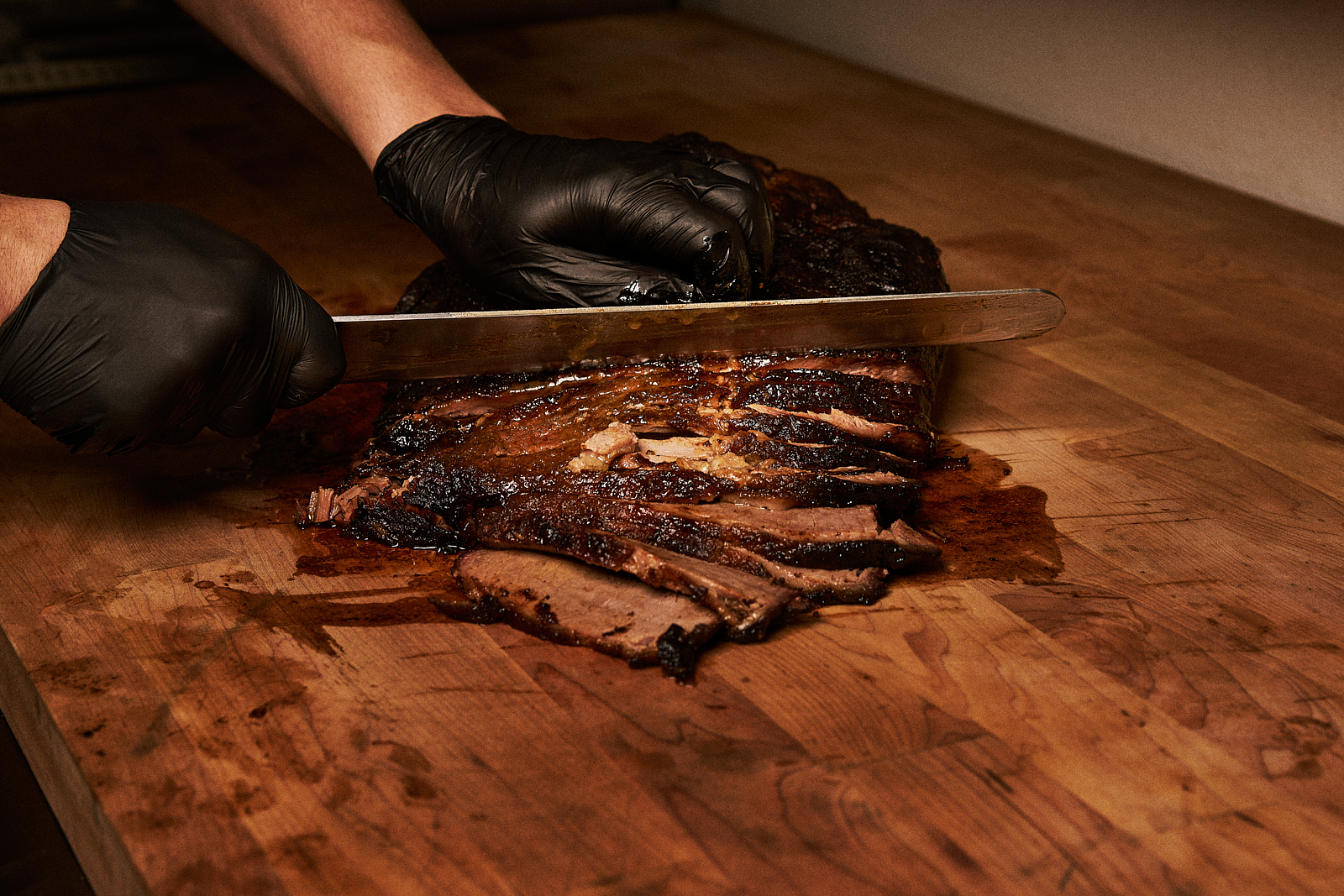 Chef slicing smoked brisket on wooden cutting board for fusion BBQ dish