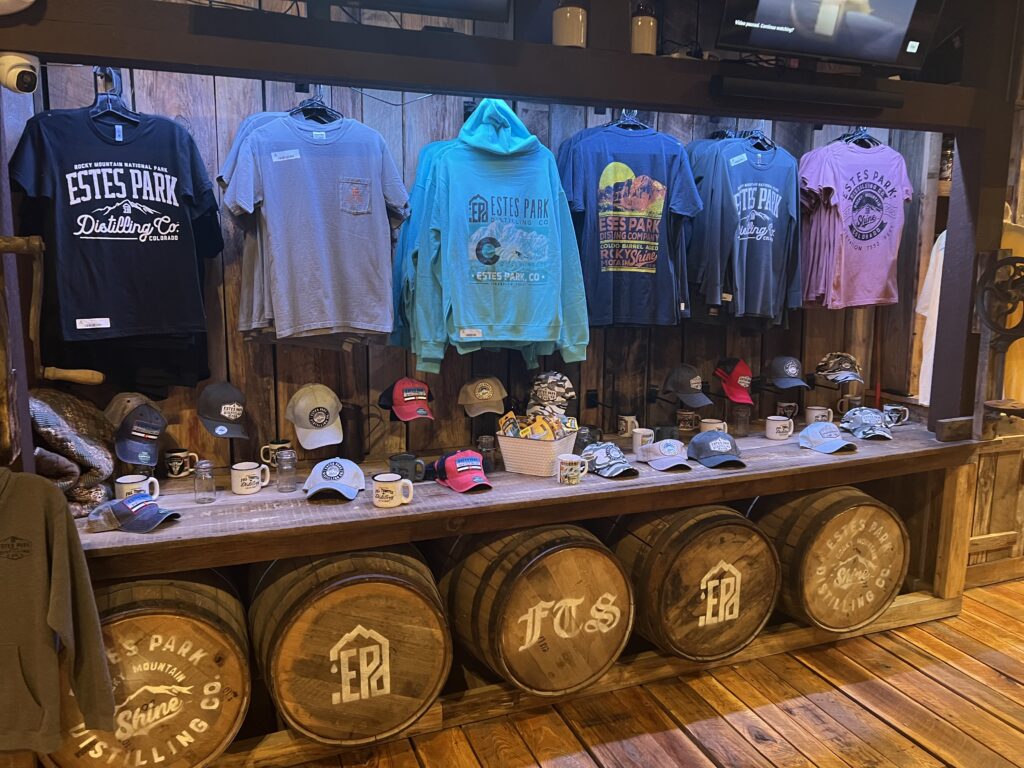 Estes Park Distillery Merch and Apparel Estes Park distillery branded shirts, hats, and mugs displayed on wooden wall