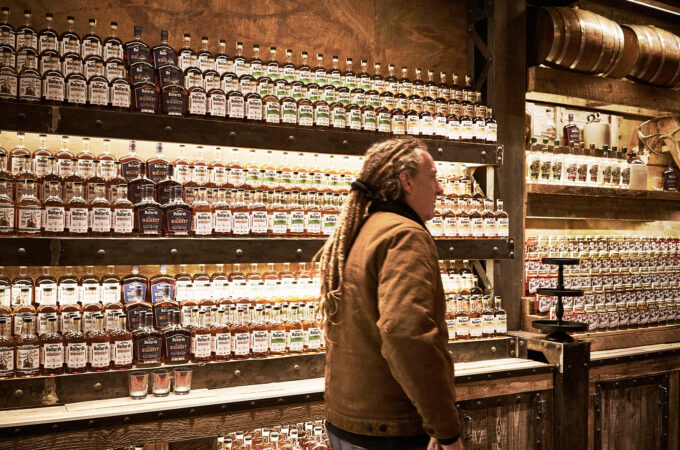 Michael Ballard inside Full Throttle Distillery in Deadwood, SD, surrounded by handcrafted moonshine and whiskey bottles