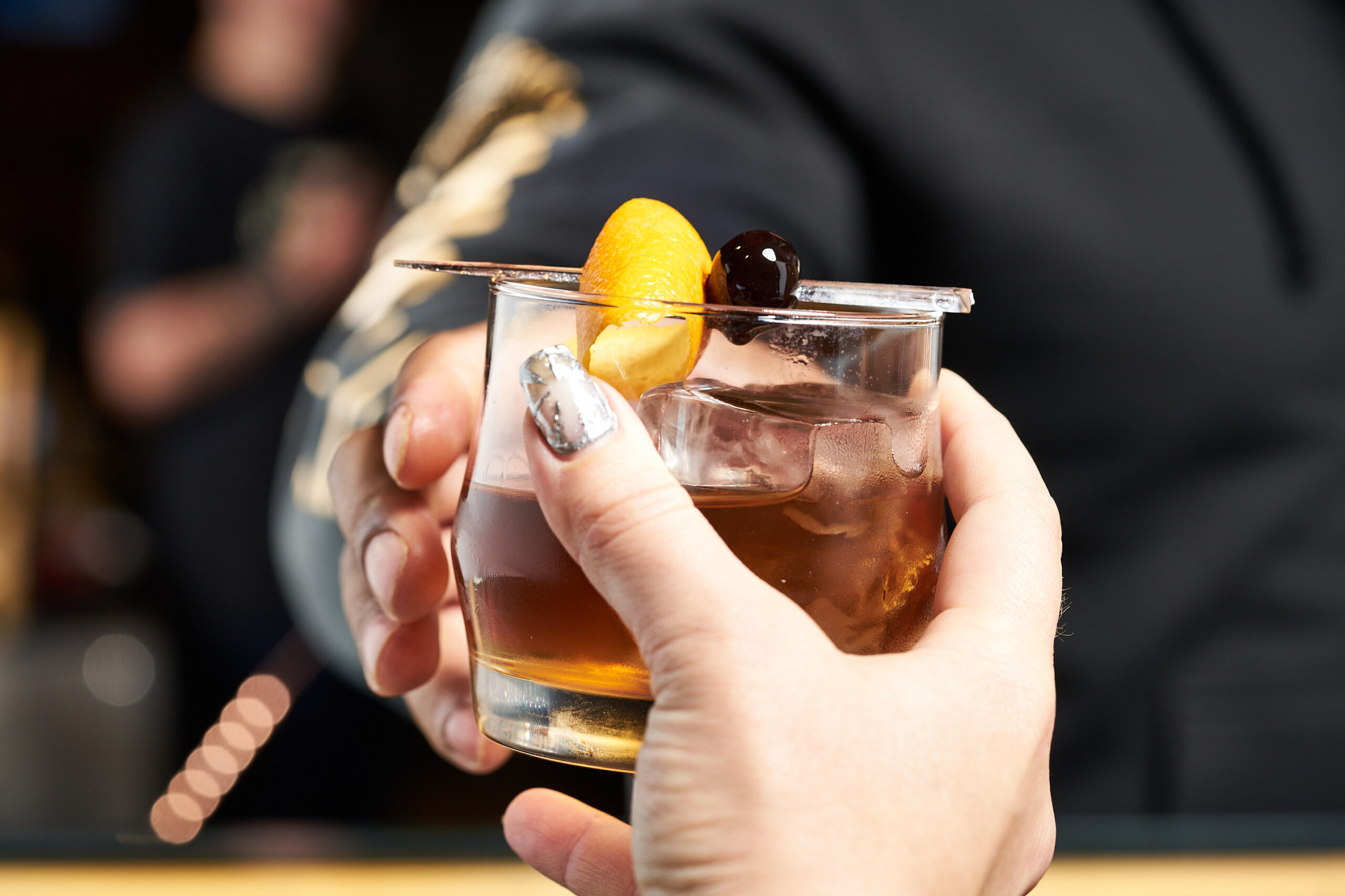 Hand holding a whiskey cocktail with orange peel and cherry garnish – drink ideas from Full Throttle Distillery