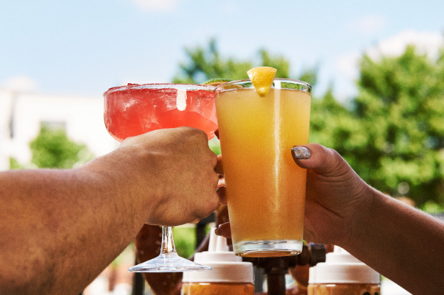 A couple clinking glasses with a margarita and a pint, celebrating a great date at Full Throttle Distillery.