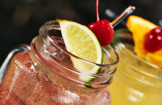 Two mason jar cocktails, garnished with a lime wedge and cherries, for happy hour at Full Throttle Distillery.