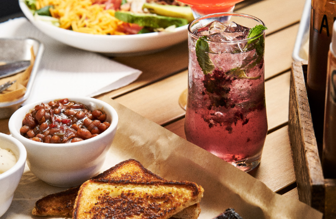 Close-up of smoked meat sides, toasted bread, and a craft cocktail on an outdoor patio table, perfect for a cozy Fall at Estes Park meal.