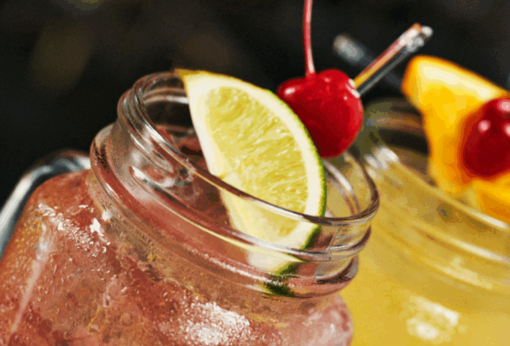 Two colorful mason jar cocktails with cherry and lime garnishes, perfect drinks for a fun date night in Branson.