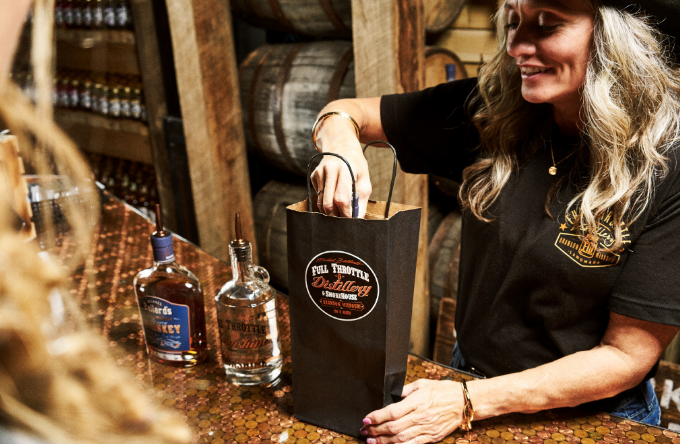 A staff member bagging merchandise or spirits at the distillery bar, offering a unique souvenir from a Date at Full Throttle Distillery.