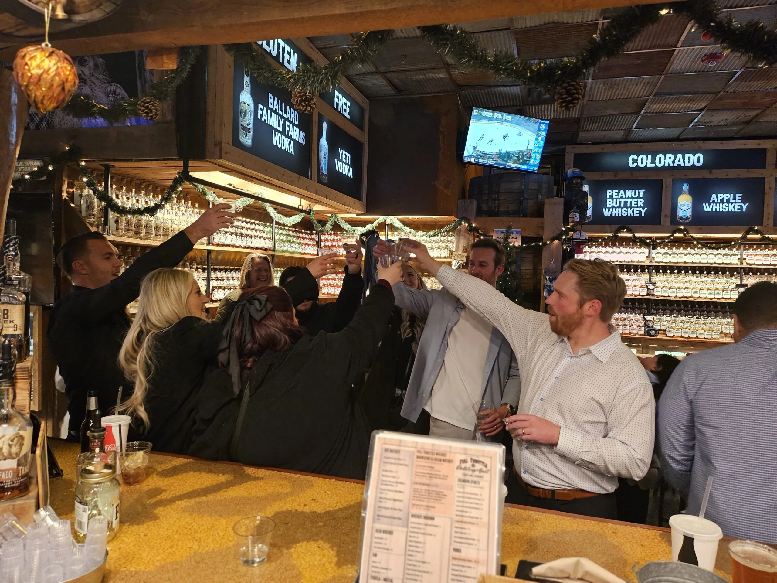 Group toasting at the bar inside Full Throttle Distillery event space with whiskey and festive decor.