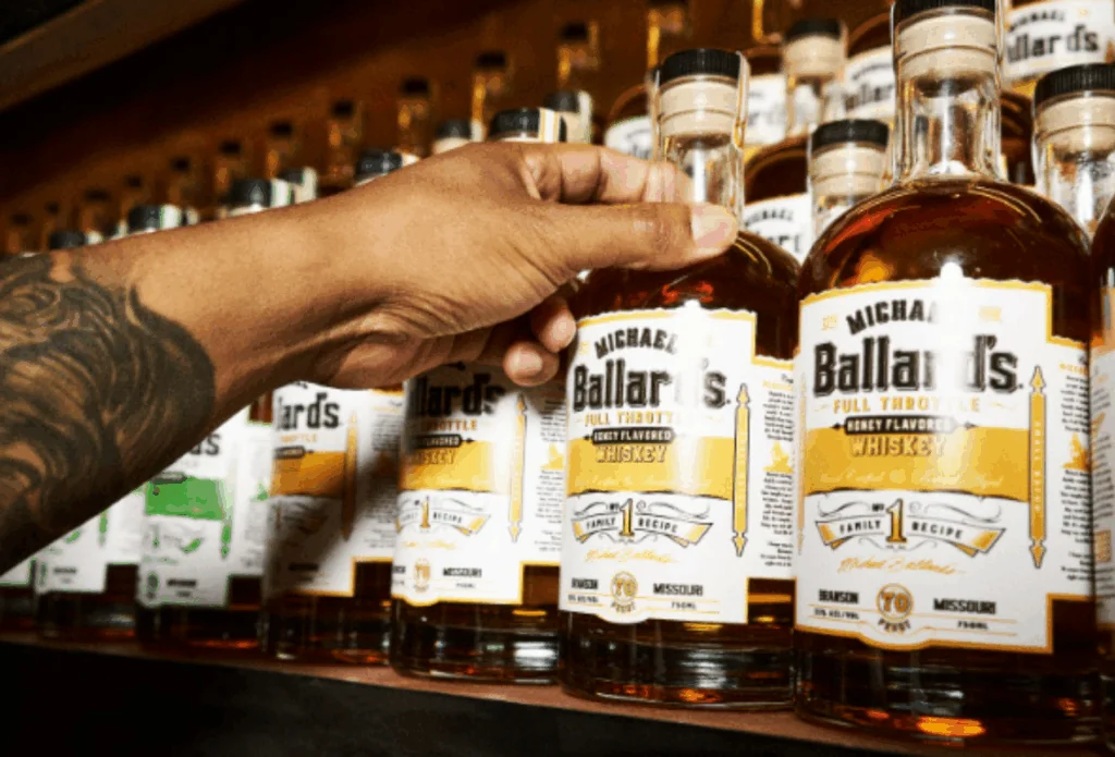 A tattooed hand reaching for a bottle of Michael Ballard's Full Throttle Honey Flavored Whiskey, ideal for gift ideas for the holidays.